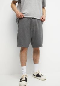 Shorts gris en mélange de coton avec taille à cordon, poches latérales, et coupe décontractée, associés à des chaussettes blanches et des chaussures noires.