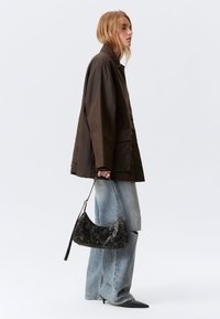 Brun letvægtsjakke, slidte lyseblå jeans, sort tekstureret håndtaske og sorte spidse hæle, stylet i en sideprofil.