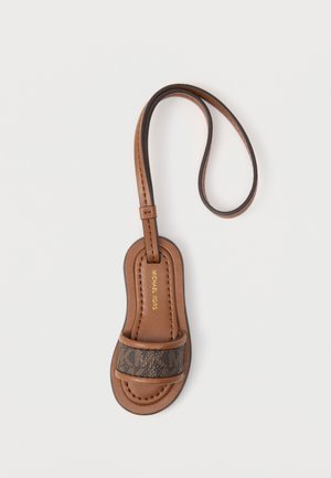 Brązowy brelok do kluczy w kształcie sandała Michael Kors z pętlą, z przednim paskiem w monogramowy wzór i złotym logo wewnątrz.