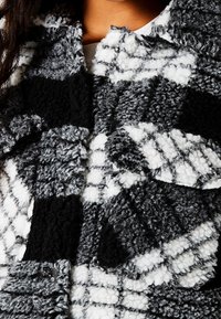 Chaqueta de cuadros en tonos negro, blanco y gris, tejido texturizado con una superficie suave y peluda, que presenta un cierre de botones y un diseño en capas.