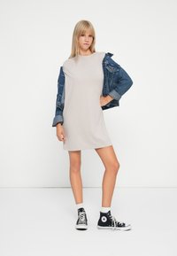 Beige cotton t-shirt dress with a relaxed fit, paired with a blue denim jacket, and black high-top sneakers with white accents.