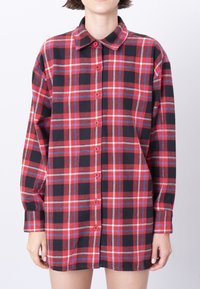 Rød og sort ternet skjorte med lange ærmer og krave. Har røde knapper og en blød, vævet tekstur.