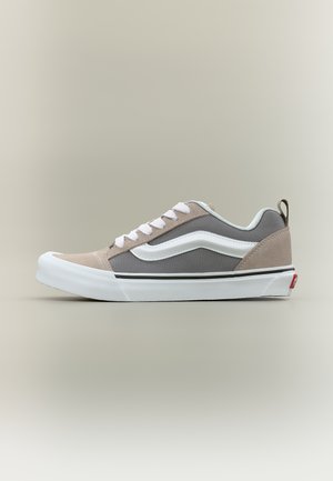 Niskie trampki z szarego płótna, beżowymi zamszowymi akcentami, białą gumową podeszwą, białymi sznurowadłami i białym paskiem bocznym na neutralnym tle.