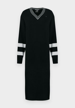 Svart strikket kjole med lange ermer, V-hals, hvite stripedetaljer på ermene, samt ribbestrikkede mansjetter og kant. Har logodetalj på brystet.