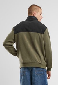 Fleece jacket with high collar; features olive green body and black upper section; soft texture and casual fit.