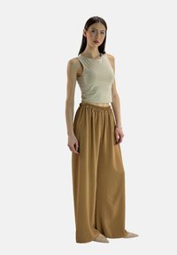 Top corto beige senza maniche abbinato a pantaloni marroni a vita alta e gamba larga. Tessuto liscio e design semplice, con una vita elastica.