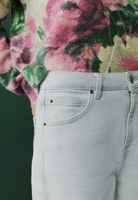 Ljusblå denimjeans med hög midja, med framfickor och subtila sömnadsdetaljer, matchade med en blommönstrad tröja.
