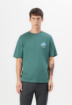 T-shirt en coton vert à manches courtes et décolleté rond, avec un petit motif graphique bleu et blanc sur la poitrine.