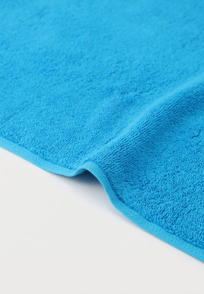 Φωτεινό μπλε ύφασμα μικροϊνών με ορατή υφή και διπλωμένη άκρη πάνω σε απλή λευκή επιφάνεια.