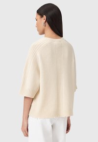 Maglione lavorato a maglia di colore crema con una vestibilità ampia, maniche corte, texture a coste e dettagli delle cuciture lungo la schiena.