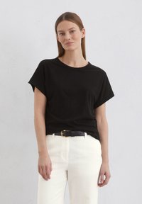 Svart kortärmad t-shirt med avslappnad passform och rundad halsringning, i kombination med vita högmidjade byxor och ett svart bälte med guldspänne.