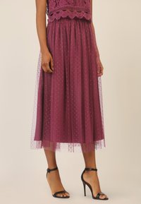 Paarse tule rok met stippenpatroon, kant tailleband en een vloeiende silhouet. Draagt met zwarte bandjeshakken.