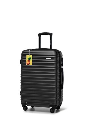 Black hard-shell suitcase with vertical ridges, retractable handle, and four wheels. Features a yellow tag with a pineapple design attached.