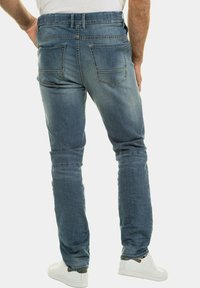 Vaqueros de mezclilla azul con un corte ajustado, diseño de cinco bolsillos y un ligero desgastado. Los bolsillos traseros tienen un acento de doble costura.