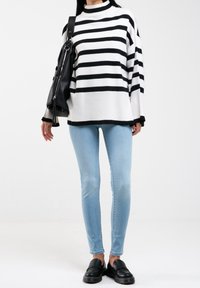 Svart och vitrandig stickad tröja med hög krage, ihop med ljusblå åtsittande jeans och svarta loafers. Svart handväska över axeln.