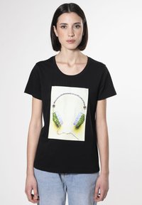Camiseta de algodón negra con un gráfico de auriculares adornados con cristales verdes y azules, sobre un fondo amarillo.