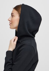 Black hooded sweatshirt with a smooth texture, featuring a drawstring and a fitted cut, shown from the side with a focus on the hood.