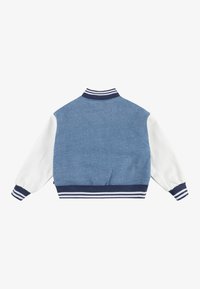 Džínová bunda s modrým zadním dílem, bílými rukávy a námořnickými pruhovanými manžetami a límcem. Má texturovaný povrch a uvolněný střih.