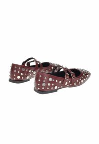 Scarpe flat borgogna con doppie cinghie a fibbia, decorate con grandi e piccoli borchie e punte, mostrate da angolazioni laterali e posteriori.