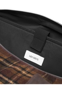 Rudos plaidinio rašto tekstilės krepšys su juodu vidumi, turintis odinį akcentą ir etiketę su užrašu "LES DEUX". Matomas užtrauktuko uždarymas.