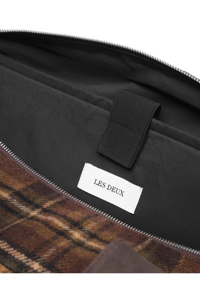 Sac textile à carreaux marron avec un intérieur noir, comportant un accent en cuir et une étiquette portant la mention "LES DEUX." Fermeture zippée visible.
