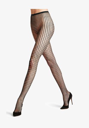 Persoon met zwarte, met patronen bedekte visnetpanty's en zwarte hoge hakken, benen gekruist, op witte achtergrond.