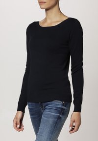 Dunkelblauer Langarmpullover mit Rundhalsausschnitt, aus weichem Stoff gefertigt. Enganliegendes Design mit gerippten Bündchen und Saum, kombiniert mit blauen Jeans.