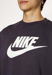 Dark purple Nike sweatshirt featuring a large white logo with a swoosh design. The fabric appears soft with a crew neck cut.