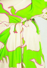 Loszittende jurk in crème met grote, felgroene bloemmotieven omlijnd met roze. Gemaakt van lichtgewicht stof met een zachte textuur.