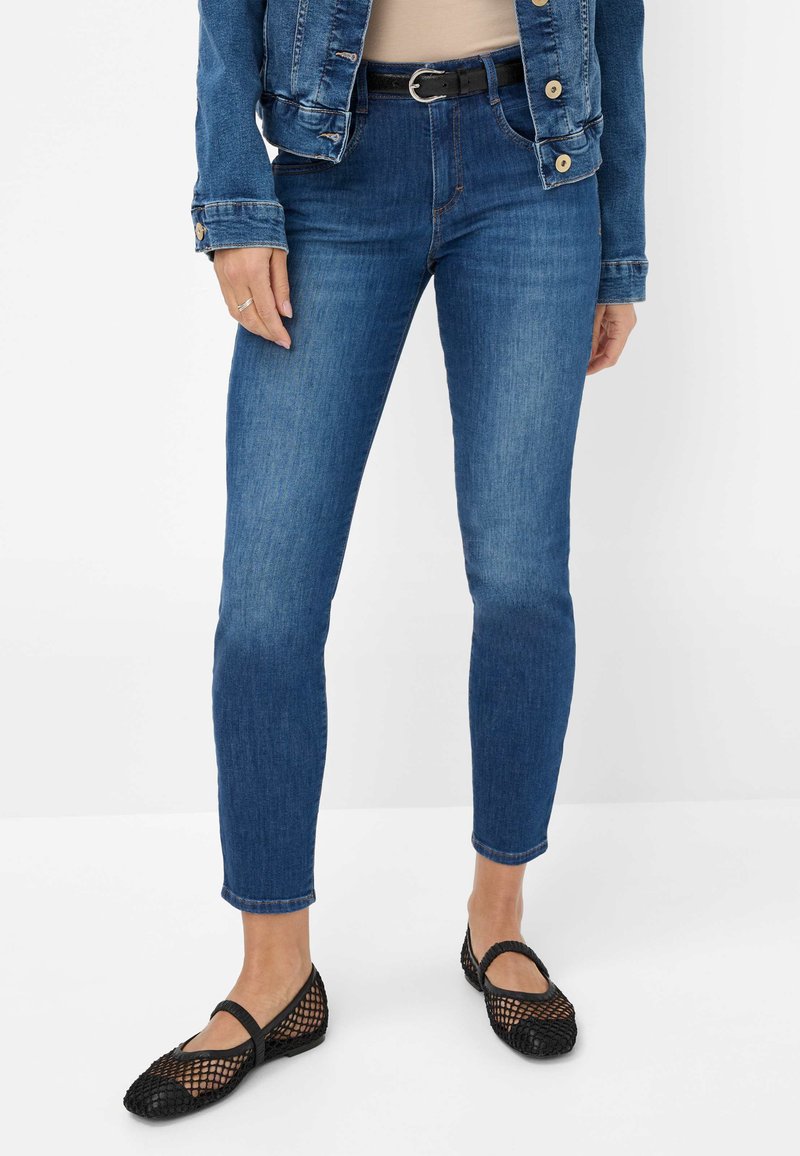 Slinker blauwe denim jeans met een middelhoge taille. Gecombineerd met zwarte mesh flats met een ronde neus. De outfit wordt aangevuld met een denimjack.