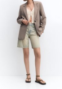 Brązowa marynarka, beżowy dzianinowy crop top, jasnoniebieskie szorty dżinsowe, brązowe sandały. Gładkie faktury i luźny krój. Minimalistyczny design.