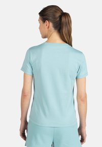 Svetle modré tričko s krátkým rukávem, kulatý výstřih, hladká textura, nošeno s odpovídajícími šortkami. Žádné viditelné logo ani vzory. Čistý design.