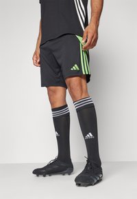 Adidas svarte shorts med grønne striper, kombinert med svarte fotballsokker med hvite striper og svarte fotballsko.