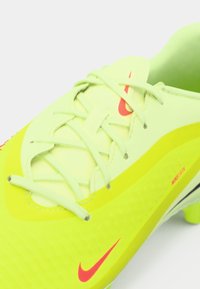 Zbliżenie na neonowożółte korki piłkarskie Nike z jasnoniebieskimi sznurowadłami, czerwonymi logo Swoosh i teksturowaną powierzchnią.
