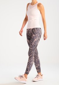 Ljusrosa ärmlös topp med mesh-krage, matchat med högmidjade leggings med mörk bakgrund och rosa bladmönster. Ljusrosa sneakers.