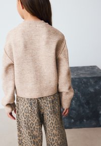 Bézs színű kötött pulóver bordázott nyakkivágással, széles szárú, barna leopárdmintás nadrággal, amelyen két hátsó zseb található.