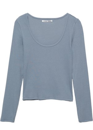 Top lung cu mânecă lungă, de culoare albastru deschis, din țesătură ribbed, cu un decolteu larg și un tiv scurt. Fără modele sau accesorii vizibile.