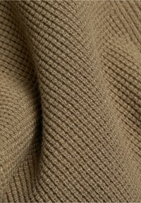 Gros plan sur un tissu doux brun avec une texture détaillée en maille côtelée et des plis visibles.