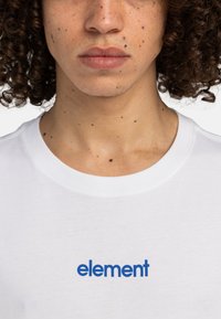 White cotton t-shirt featuring a round neckline and blue "element" logo on the chest. Smooth texture with a classic fit.