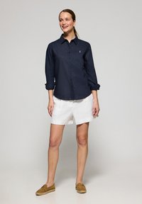 Navy blue button-up shirt with rolled sleeves, white linen shorts, and brown moccasin shoes. Simple design, no patterns or embellishments.