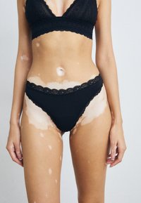 Black lace-trimmed bralette and matching high-waisted briefs. The fabric appears soft with a delicate floral pattern along the edges.