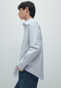 Jasnoniebieska koszula z długim rękawem, wykonana z bawełny, z kołnierzykiem w kształcie punktu i prostym dołem, w zestawie z ciemnoniebieskimi dżinsami.