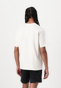 Cremefarvet bomulds t-shirt med afslappet pasform, korte ærmer og rund hals, parret med mørke mønstrede shorts.