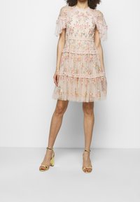 Robe rose à broderies florales avec des manches à volants, conception en étages, et une texture légère. Associée à des sandales à talons bloc dorées.