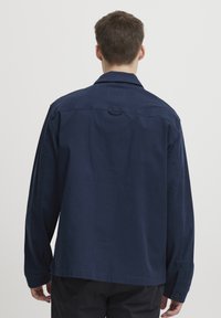 Navy blue long-sleeve shirt with a collar, back yoke, and buttoned cuffs. Made of smooth fabric with a straight cut and no visible patterns.