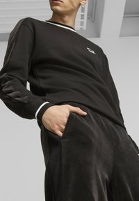 Sudadera negra con detalles en blanco y escote en forma de V, combinada con pantalones de velour negros con bolsillos laterales y un corte relajado.