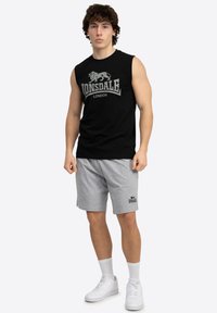 Juodas be rankovių marškinėliai su balta "Lonsdale London" grafika, derinami su pilkais šortais su logotipu, avimi baltais sportbačiais ir kulkšnies kojinėmis.
