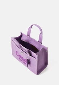 Purple canvas handbag featuring a stitched "Coach New York" logo, zippered pocket inside, and dual top handles. Textured fabric finish.