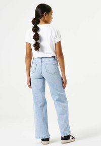 Lichtblauwe jeans met hoge taille en rechte pijpen, voorzien van achterzakken en een wit T-shirt. Zwart-witte sneakers maken de look compleet.