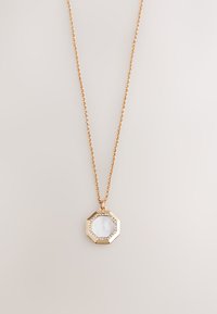 Gold chain necklace with an octagonal pendant featuring a white mother-of-pearl center and small sparkling stones around the edge.